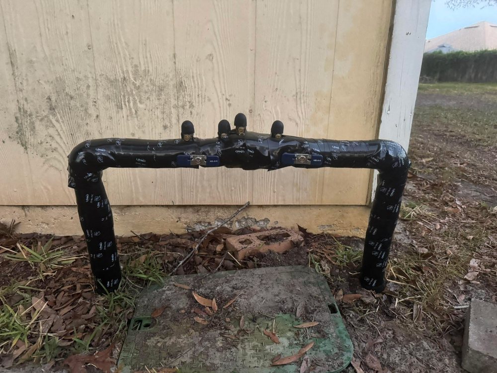 Backflow preventer wrapped in black insulation tape beside a valve box